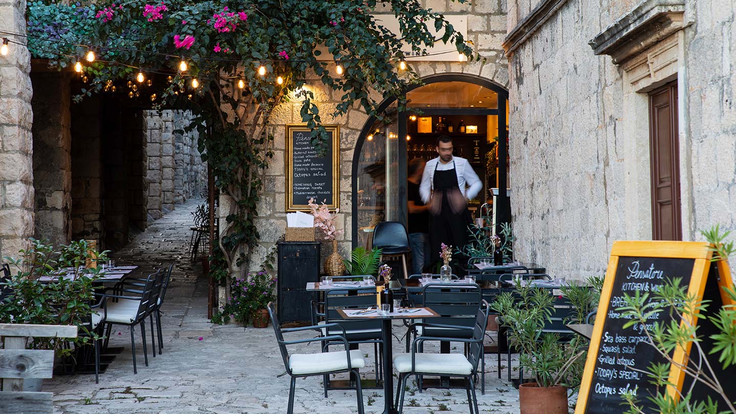 En charmig gränd med uteservering i Korčula stad, Kroatien, med växter och belysning.