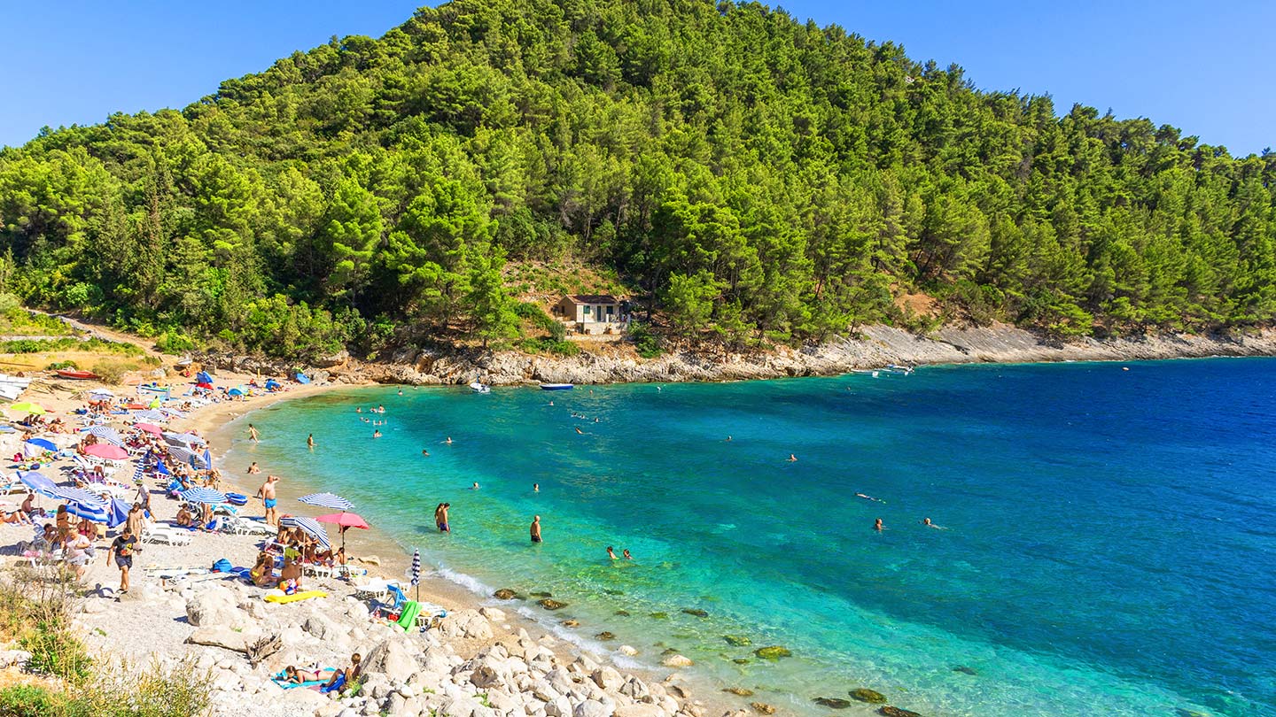 Stranden i Pupnatska Luka på ön Korcula i Kroatien, med klara vatten och solande besökare.