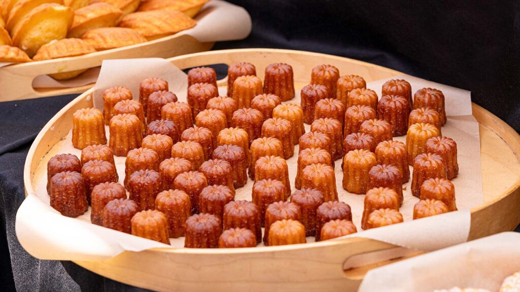 En plåt med mini canelés de Bordeaux, gyllene och mörka, vackert arrangerade.