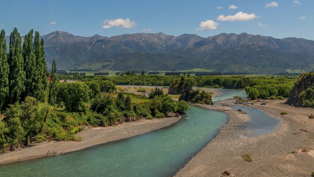 Waiau Uwha floden flyter genom grönskande landskap vid Hanmer Springs. Magnifika berg i bakgrunden.