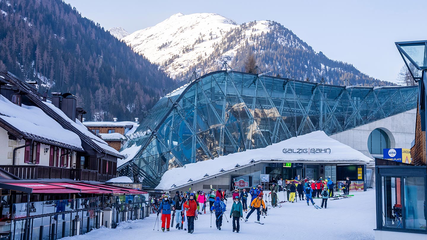 Dalstationen för Galzigbahn, skidåkare samlas i St. Anton am Arlberg. Snöklädda berg.