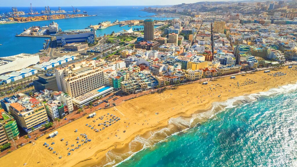 Bilden visar Playa de Las Canteras i Las Palmas, Gran Canaria, med gyllene sand och blått hav.