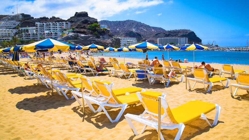 Stranden Playa de Puerto Rico på Gran Canaria med solstolar och parasoller.