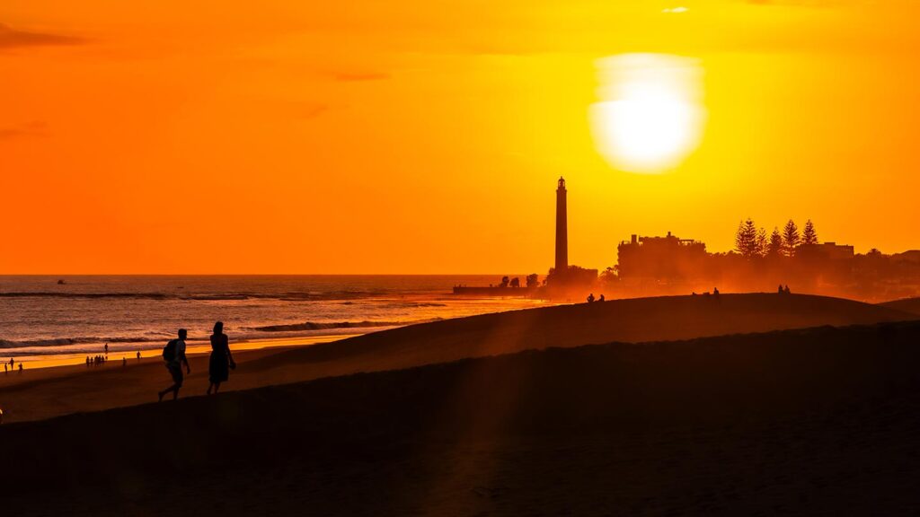 Turister går på sanddyner vid Maspalomas under en vacker solnedgång.