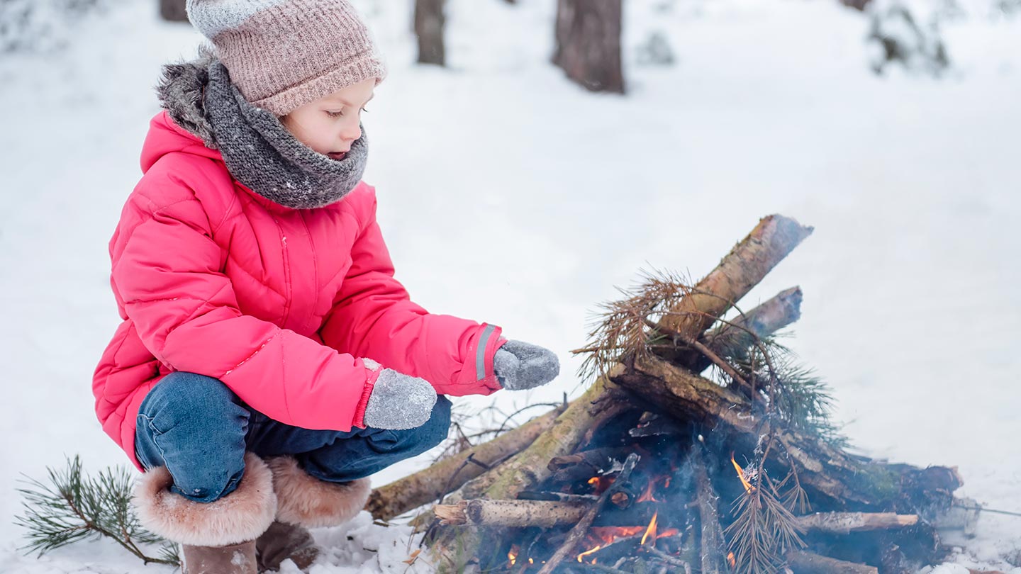 Ett barn sitter vid ett eldläger i snön i Härjedalen, Sverige.