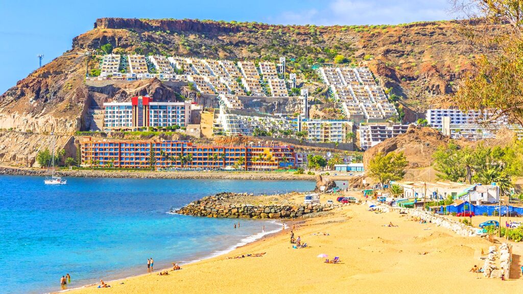 Vacker strand i Puerto Rico, Gran Canaria, med lyxhotell och klarblått vatten.