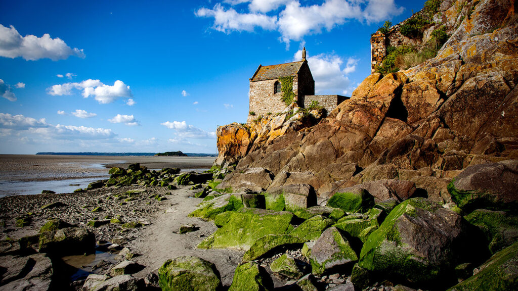 Mont Saint Michel vid Engelska kanalen, omgiven av klippor och tidvattenområden.